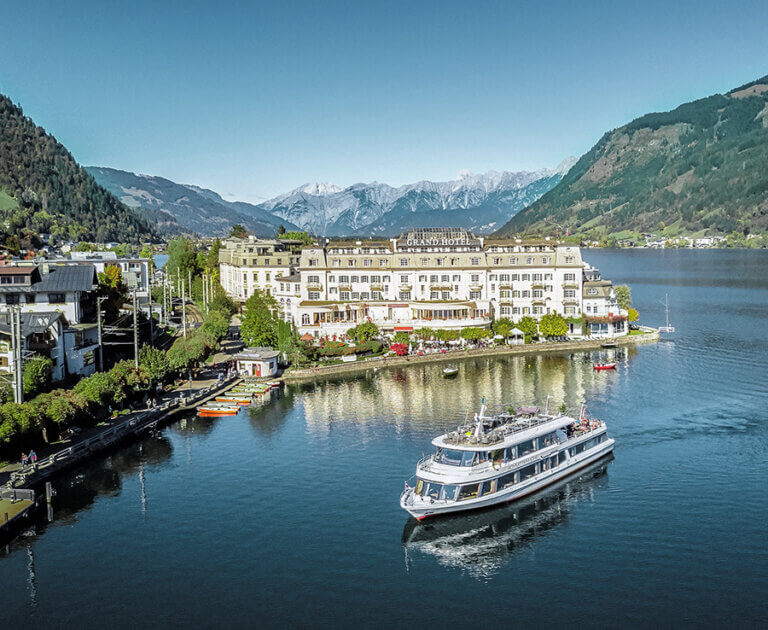 Grosses Seehotel vor Bergkulisse mit Passagierschiff.