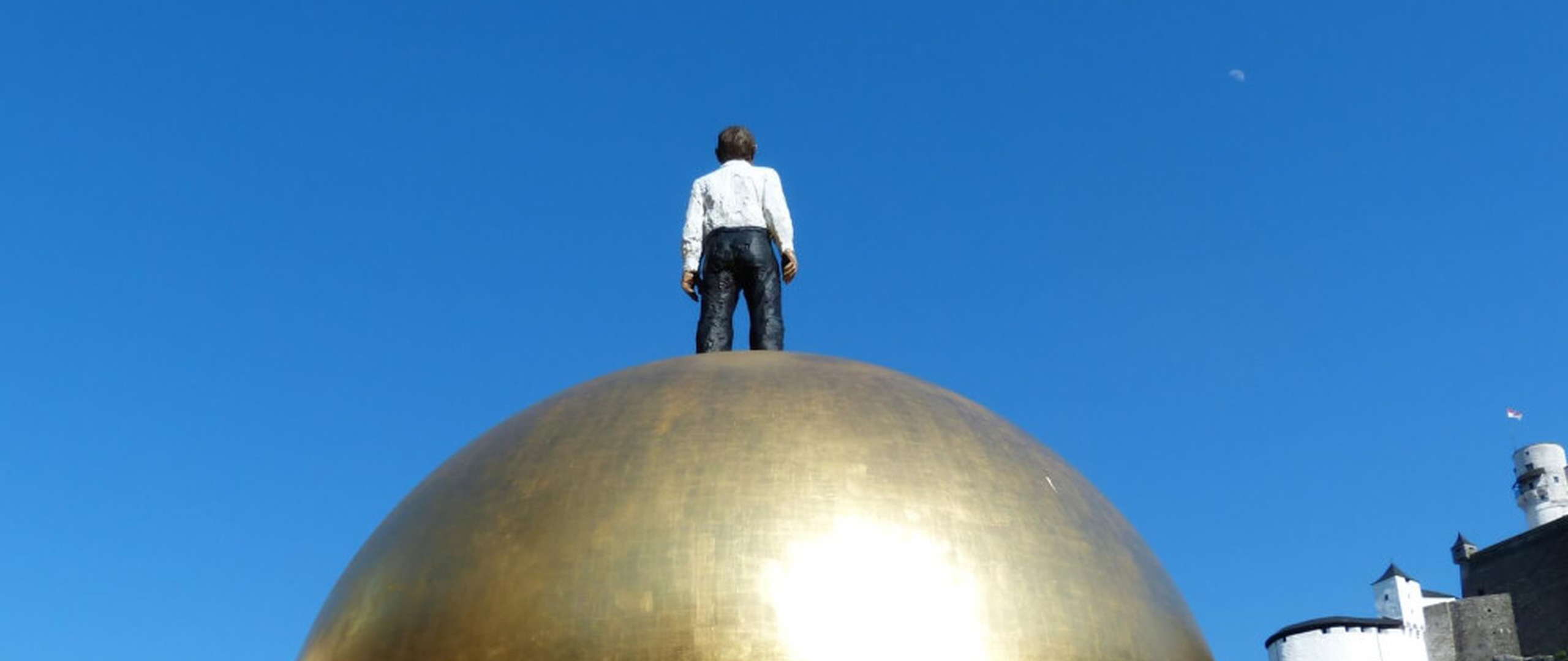 Golden Sphaera sculpture by Stephan Balkenhol at Kapitelplatz in Salzburg, Austria, with Hohensalzburg Fortress in the background.