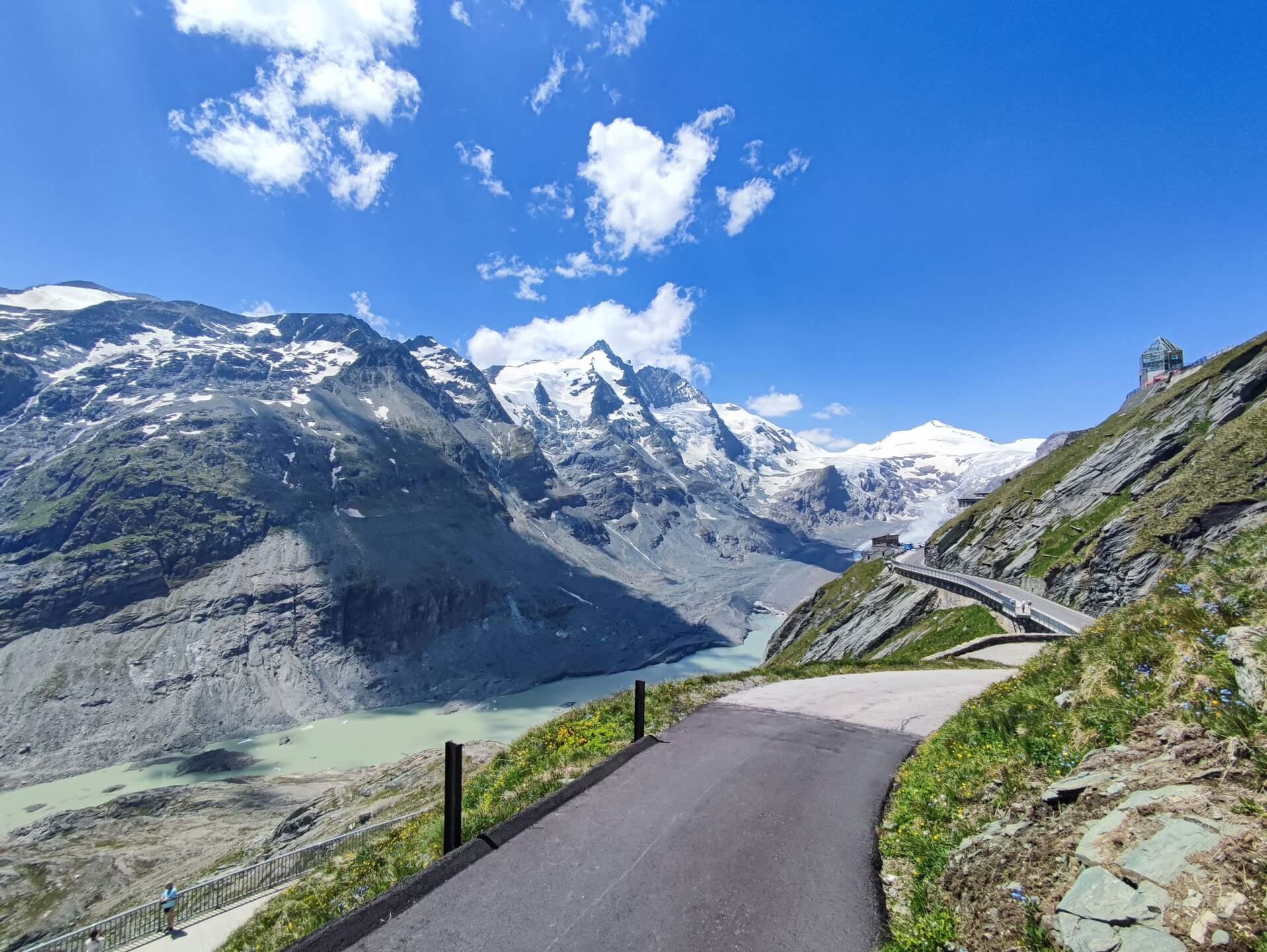 An Alpine road winding through green mountains below glacier peaks
